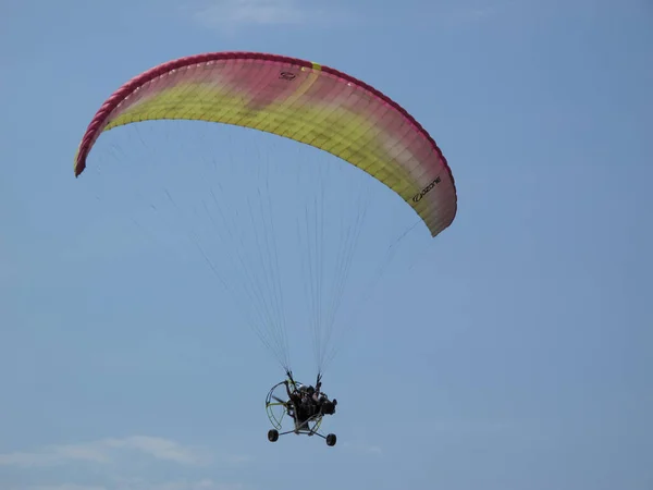 パラグライダーは多色のパラグライダーの下で空を飛ぶ 青い空の下でパラグライダーが翼の下を飛ぶ パラグライダーの演奏 — ストック写真
