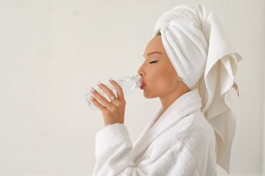 Beyaz önlüklü ve kafasında havlu olan genç bir kız şişeden temiz su içiyor..