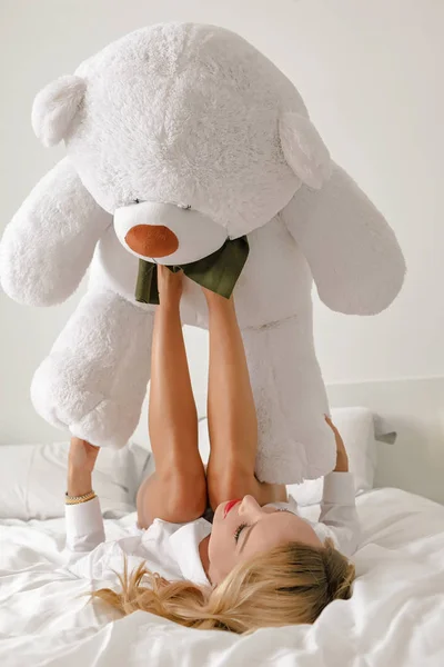 A young girl in a white shirt on the bed is playing with a white big bear toy.