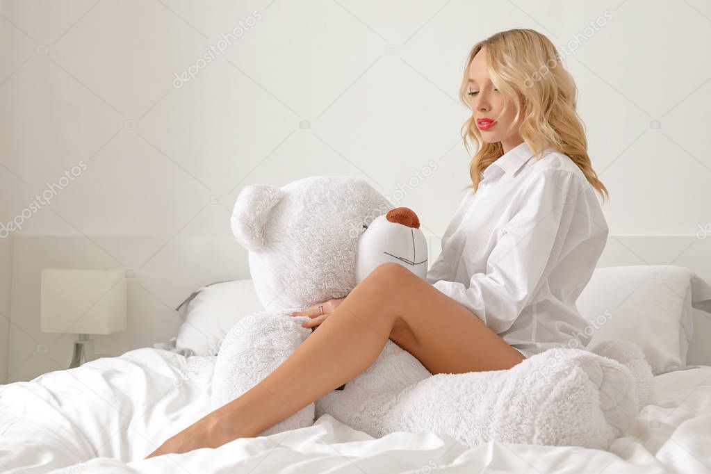 A young girl in a white shirt on the bed is playing with a white big bear toy.