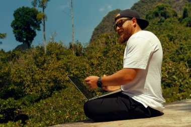 Young stylish bearded blogger working on vacation in the mountains.