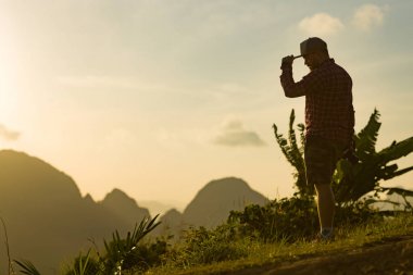 Sakallı ve şapkalı genç bir fotoğrafçı, yüksek bir dağda şafakla buluşuyor..