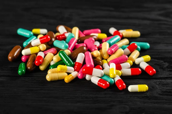 A lot of colorful pills capsules pills in a pile on a wooden table black