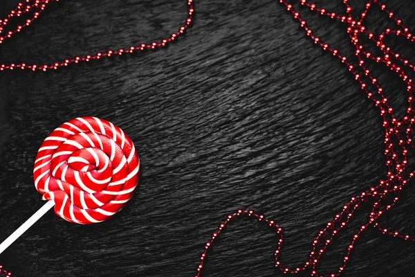 red round Lollipop on black background with texture near beads of red color