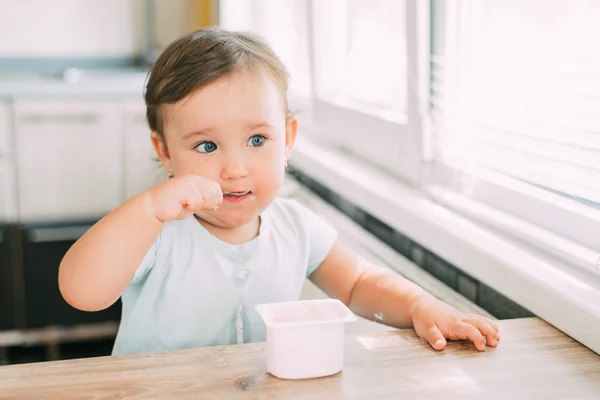 Little girl in the afternoon in the kitchen eating yogurt