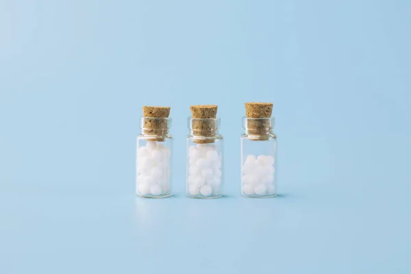 Homeopathic globules and glass bottle on blue background. Alternative Homeopathy medicine herbs, healtcare and pills.