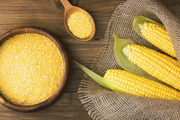 Corn grits in a wooden bowl on the background of fresh corn on the cob on a burlap.