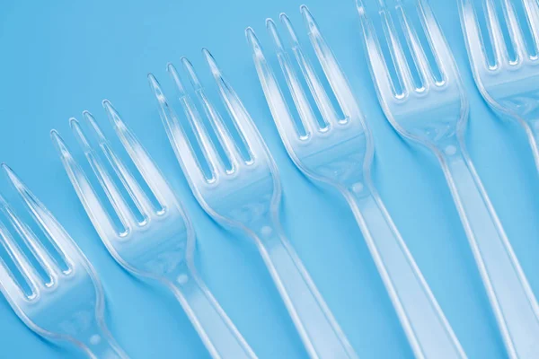 Plastic disposable tableware, cutlery. Fast food. Clean plastic forks on blue background. Disposable dishes, environmental pollution.