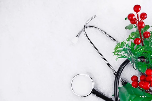 Medical stethoscope on a snowy background near a Christmas branch. Medical concept for Christmas or New Year. Flatly. Copy space