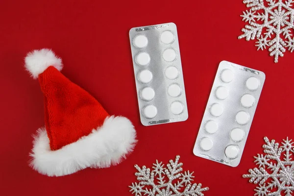 Medical Christmas background. Pills, blister and santa claus hat,on a red background with snowflakes. Flatly. Copy space