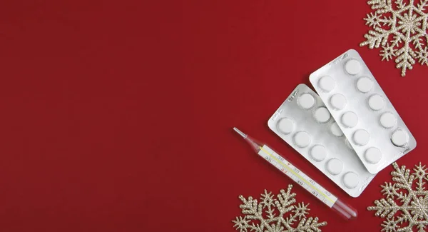 Medical Christmas background. Pills, blister and thermometer,on a red background with snowflakes. Flatly. Copy space