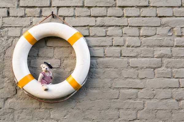 レンガの壁の背景にあるヴィンテージライフブイとかわいいテディベアは 懐かしい水夫の水着を身に着けています コピースペース ロイヤリティフリーのストック写真