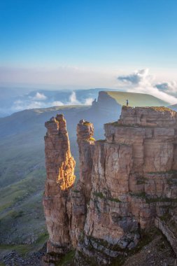 Dağlarda şafak, manzara. Dik bir çıkıntıda küçük bir insan figürü görülüyor..