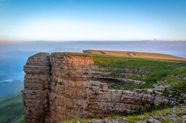 Şafakta dağ manzarası. Dik bir uçurum güneş ışınları yla aydınlanır. Sisteki ufuk.