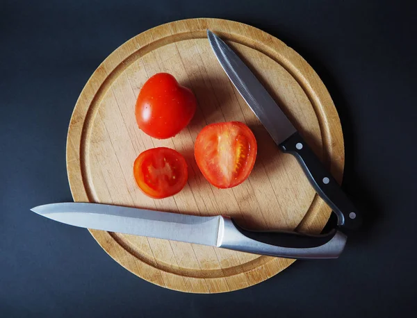 Tomatoes on the round wooden cutting board with two knives