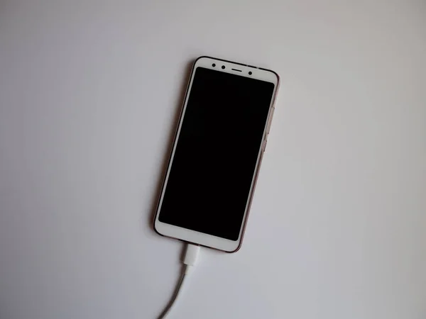 A smartphone with a white USB cable for charging