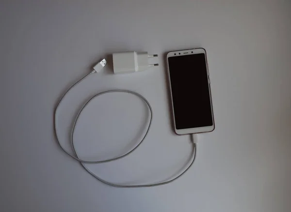A smartphone with a white USB cable for charging