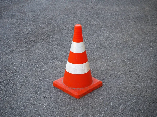 Red and white striped traffic cone on an asphalt road. It is used as a fence when carrying out road-building works, for demarcating traffic or for designating emergency sites and road accidents