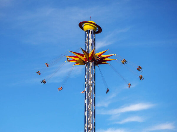 Saint-Petersburg, Russia. 06.23.2019. Divo Ostrov Amusement Park on the Kresovsky Island. People in motion on the high whirling extreme attraction 'The Seventh Heaven' (Ride Star Flyer carousel) on the blue sky background. 