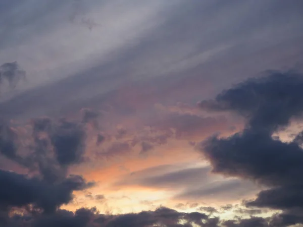 View of the dramatic sky at sunset with dark blue clouds and pink, purple and yellow flashes from the sun\'s rays