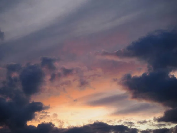 View of the dramatic sky at sunset with dark blue clouds and pink, purple and yellow flashes from the sun\'s rays