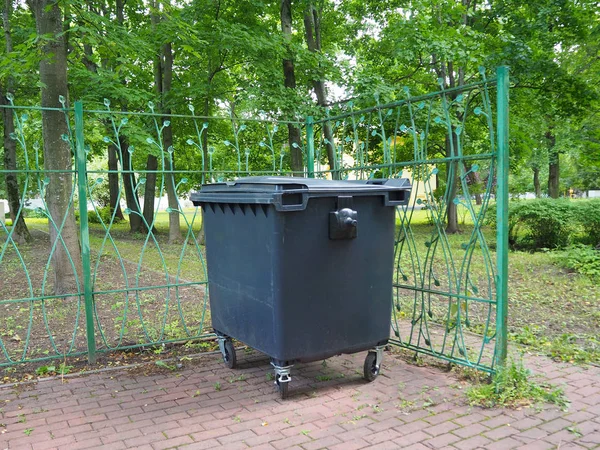 Clean city trash can in the park on green trees background. Bin for collection of recycle materials. Plastic garbage container.