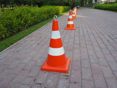 Turuncu ve beyaz çizgili trafik konileri birbirine zincirlenmiş. Yol yapım işlerini yürürken, trafiği niçin çizerken ya da acil durum ve trafik kazalarını belirlemede çit olarak kullanılır..