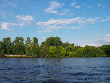 Geniş bir nehrin kıyısında yeşil ağaçların ve beyaz bulutların olduğu mavi gökyüzünün olduğu yaz manzarası