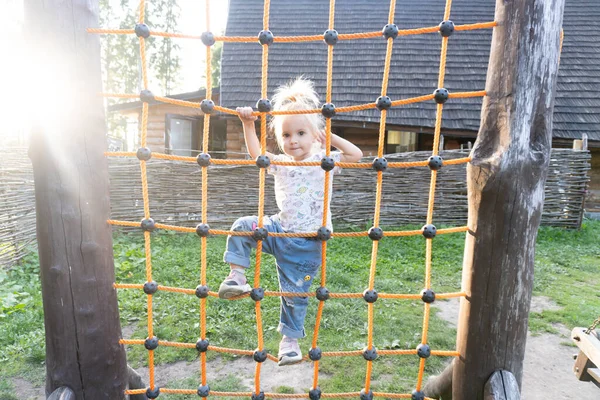 Καυκάσιο ξανθό παιδί σκαρφαλώνει στο δίχτυ στην παιδική χαρά την καλοκαιρινή μέρα — Φωτογραφία Αρχείου