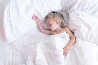 Beyaz çarşaflarla uyuduktan sonra beyaz çarşaflarla uyanan beyaz çocuk el kaldırıyor..