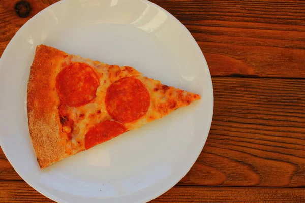 Masadaki beyaz tabakta bir dilim pizza.