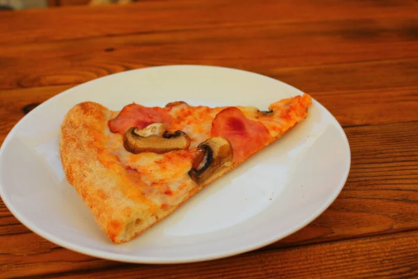 Masadaki beyaz tabakta bir dilim pizza.