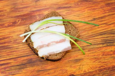 Bir parça pastırma ve yeşil soğan üstüne siyah ekmek. Ahşap bir arka planda pastırma ile bir dilim ekmek.