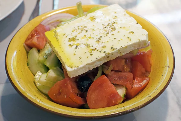 Traditional Greek salad with feta in a yellow plate. Delicious salad with cheese, vegetables and olives.