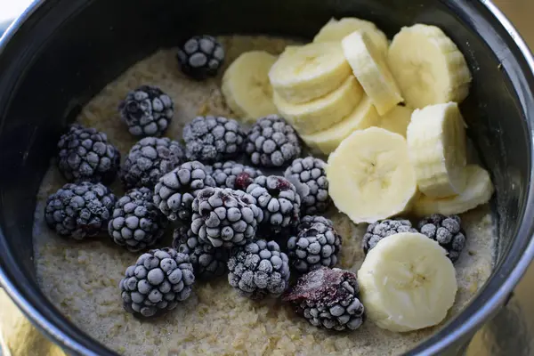 Large, ripe, frozen blackberries and bananas in a pan with oatmeal. Oatmeal with blackberries and bananas. Delicious and healthy breakfast food.