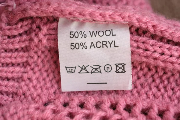 Yün yapılmış pembe örme kazak yanlış tarafı, kompozisyon belirtilir: 50% yün ve% 50 akril. Kumaş kompozisyonu pembe doku arka plan üzerinde beyaz giysi etiketi.