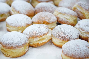 Homemade stuffed donuts on a parchment covered table. Round donuts sprinkled with white icing sugar with fruit jam. Sweet baking department in the store. clipart
