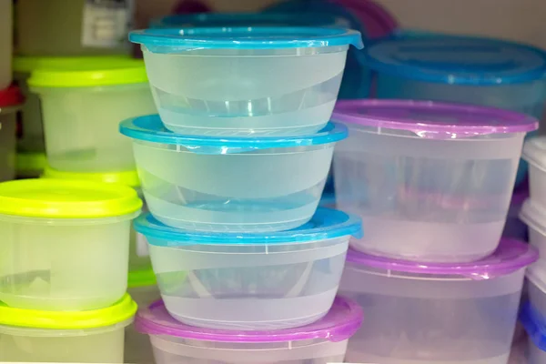 Mutfak dolabının rafındaki plastik mutfak tepsileri. Çapı ve yüksekliği farklı yuvarlak gemiler. Farklı renkte kapaklı şeffaf gıda kapları: sarı, mor, mavi.
