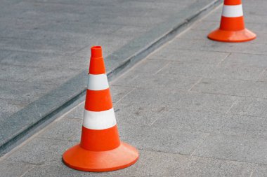 Kare gri bir fayansta iki yol konisi. Beyaz çizgili turuncu koniler. Yol inşaatı sırasında eskrim; hareketin farklılaşması; acil durum bölümlerinin belirlenmesi ve kaza noktaları