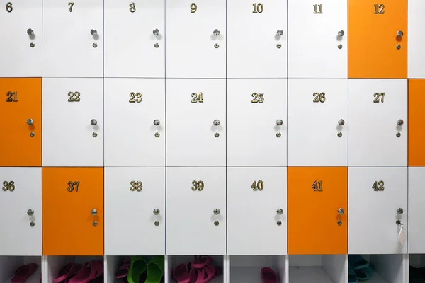 Luggage storage for things. Wooden cells in white and orange, with metal handles and locks. Cells numbered with metal numbers. All cells except one are closed. Temporary storage of things.