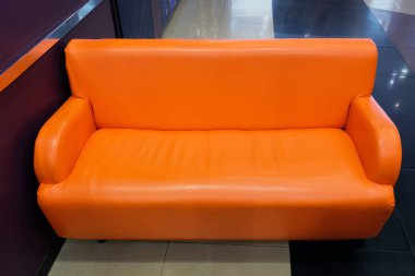 Odada minimalizm tarzında turuncu yapay deri kanepe var..