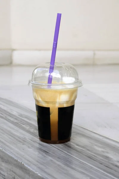 Milk brown smoothie in a plastic cup with a lid. The hemisphere-shaped lid on the glass, a purple tube. Glass with coffee on a beige wall background. Delicious cold drinks in disposable dishes.