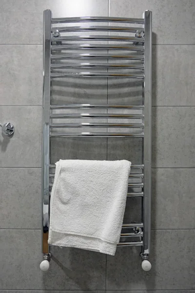 Stainless electric towel dryer for the bathroom. Drying is mounted on a wall with gray tiles, white towel. Towel dryer for drying towels in the bathroom, heating and drying the bathroom