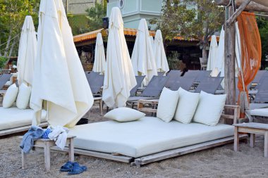 Beyaz yataklı yatak ve kumsalda yastıklar. Sandalyenin ve eşyaların yanına. Türkiye 'de deniz kenarında şemsiyeler ve dinlenme yerleriyle rahat.