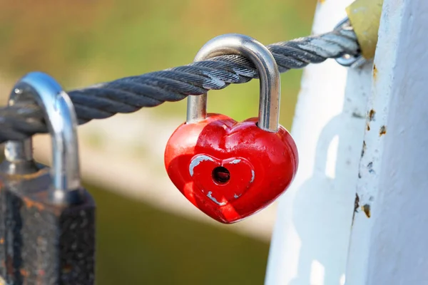 赤い鍵が橋の上のケーブルにかかっている 橋の近くに永遠の愛と忠実な金属製のハート型のロックのシンボル 結婚式の伝統 — ストック写真