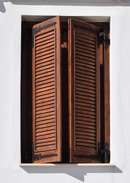 wooden window shutters of an mediterranean house. white wall with a window closed on brown shutters.