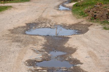 Baharda çukurları olan kırsal bir yol. Derin su birikintileri olan asfaltsız yol. Köydeki bir cadde boyunca toprak bir yolda büyük bir su birikintisi..
