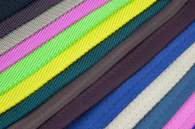 Renkli polyester kemerler, çantalar ve sırt çantaları için omuz askıları yapmak için örnek palet. Çantalar için kemer kayışı ve köpek tasması dikmek için. Çapraz katlanmış kemerlerin renkli arkaplanı.