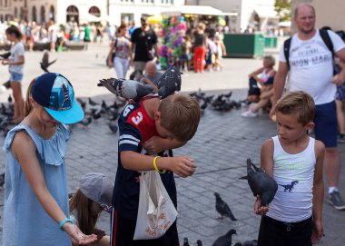 Krakow Polonya 08.2017 Çocuklar pazar meydanı Krakow güvercin beslemek. Junior büyük çocuktan sonra tekrar etmeye çalışıyor..