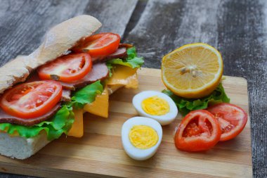 Jambonlu, peynirli, domatesli ve marullu iştah açıcı bir sandviç yumurta ve limonlu.